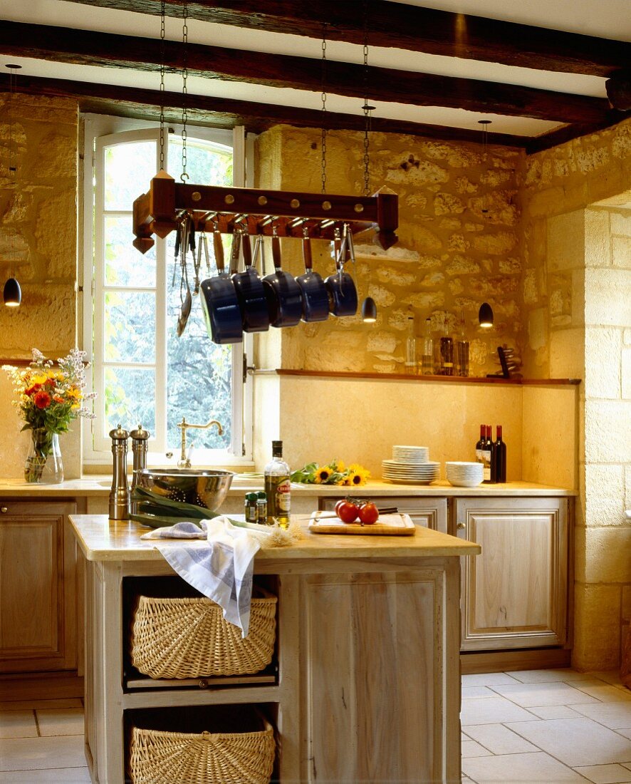 Solid wood island counter with cabinets below pans hanging from rack in rustic kitchen
