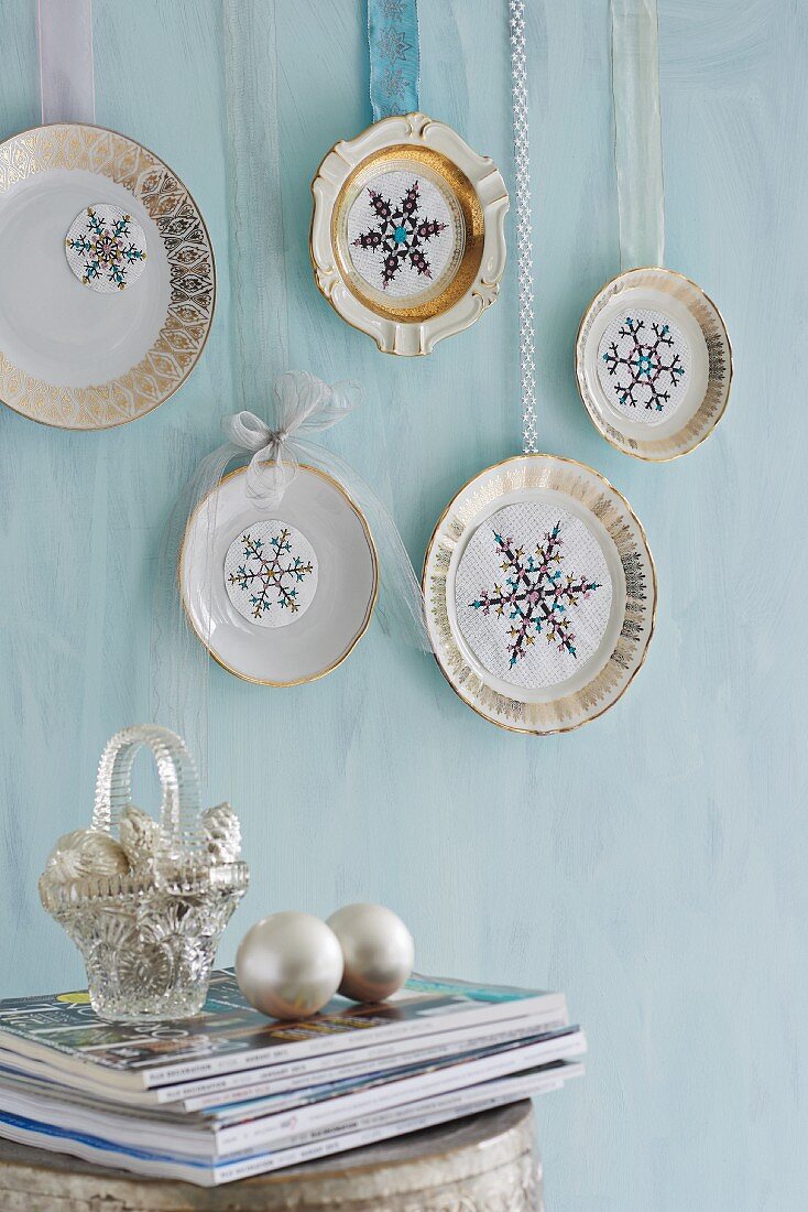 Decorative plates embellished with snowflake motifs hung from ribbons on pastel-blue wall