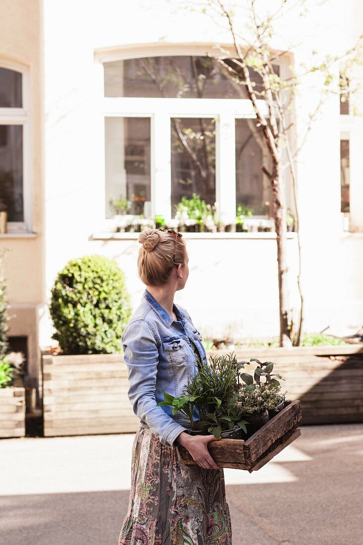 Woman carrying wooden crate of garden herbs