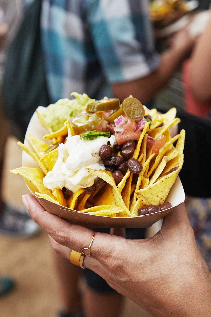 A hand holding a paper bowl of tortilla chips and beans at a market (Barcelona, Spain)