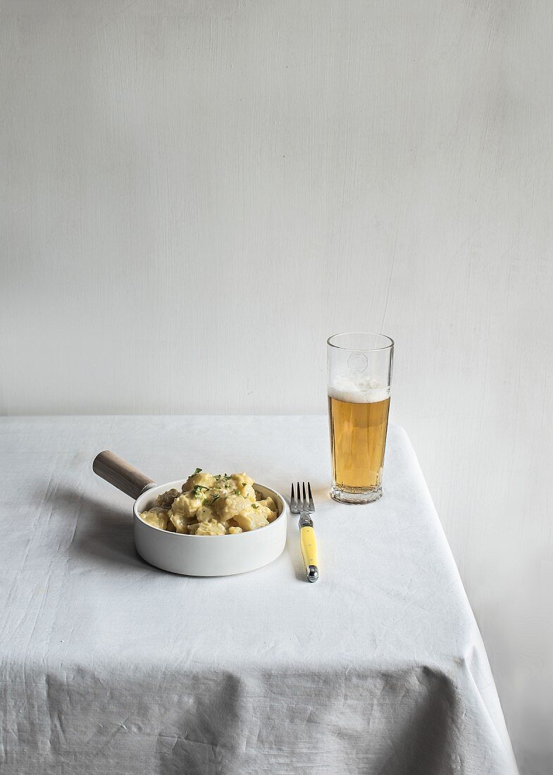 A bowl of potato salad and a glass of beer on a table