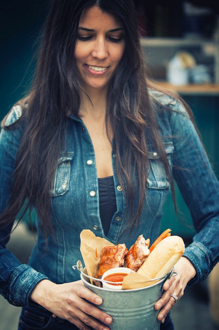 Frau mit Streetfood: Spareribs, Brot & Sauce in Metalleimer