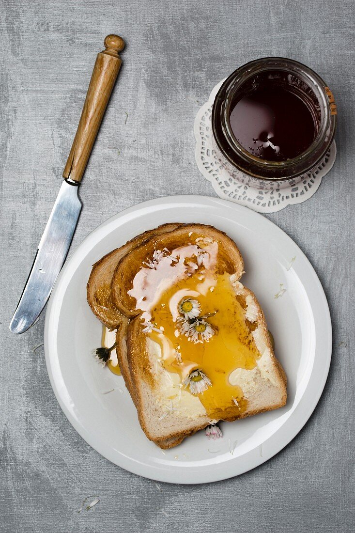 Toastbrotscheiben mit Honig und Gänseblümchen daneben Honigglas