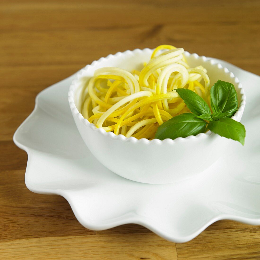 Gelbe Zucchinisppaghetti mit Basilikum in weisser Schale