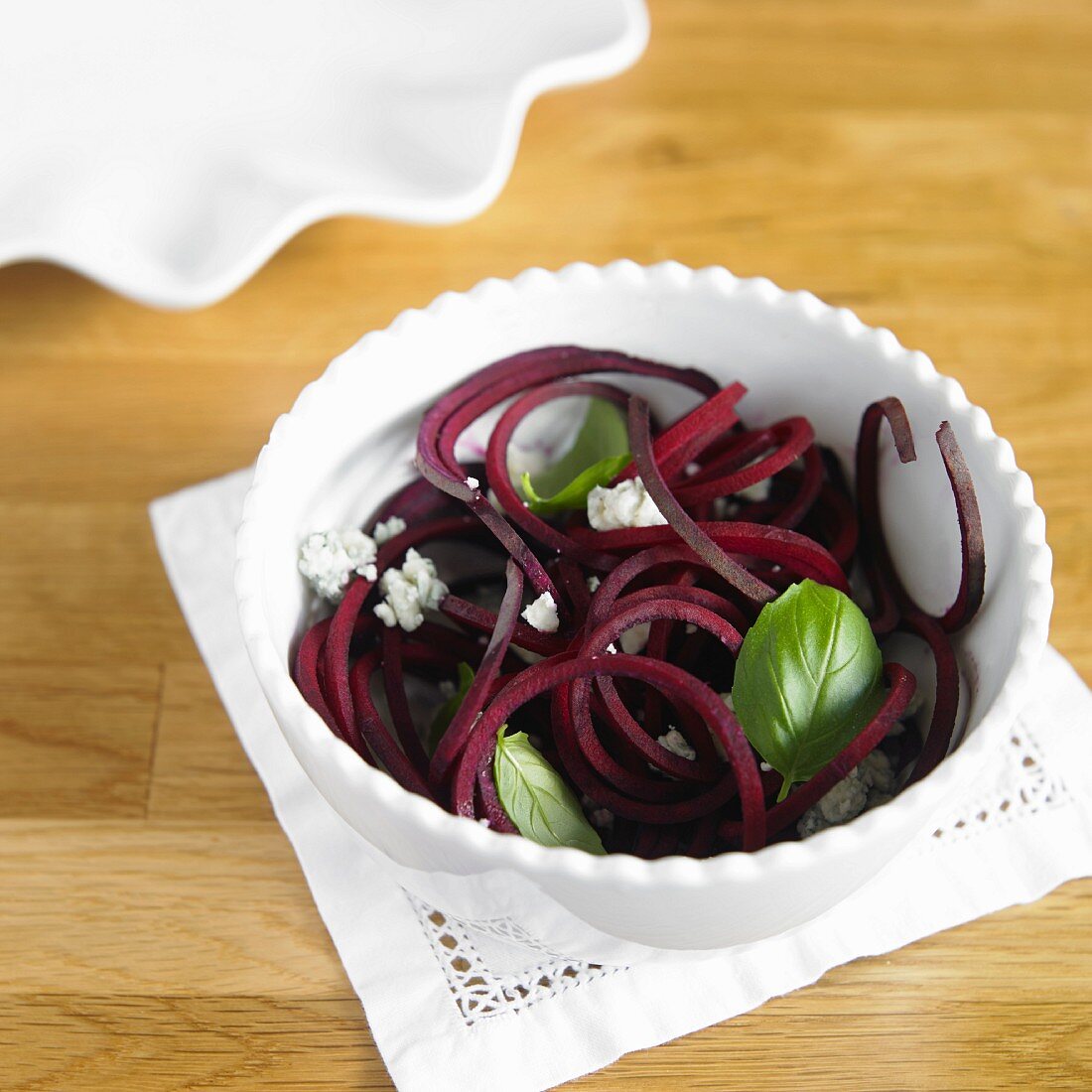 Vegetable spaghetti made from beetroot with Gorgonzola and basil in a white bowl