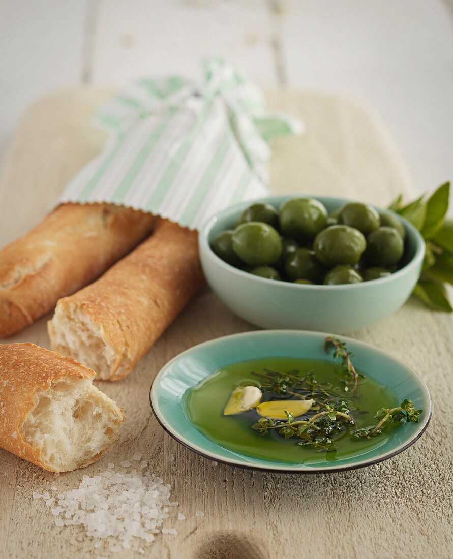Olivenöl, grüne Oliven und Baguette