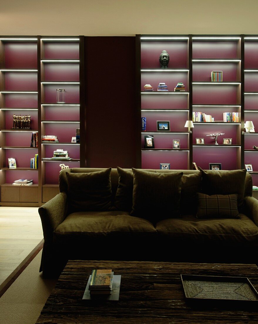 Sofa vor beleuchtetem dunklem Wandregal mit violetter Rückwand