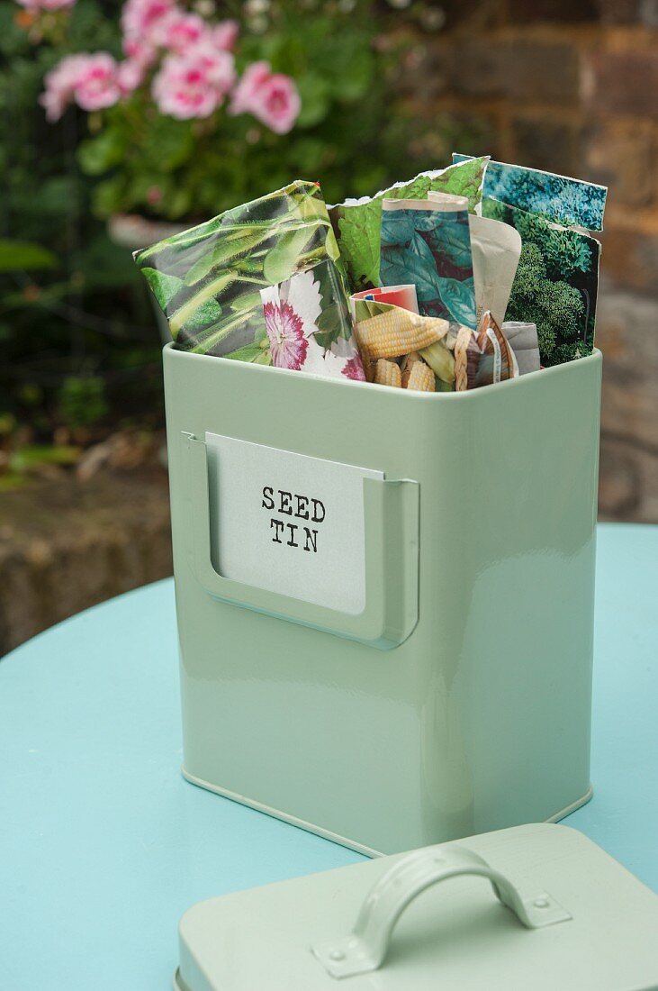 Vintage-style metal tin of seed packets on table in garden