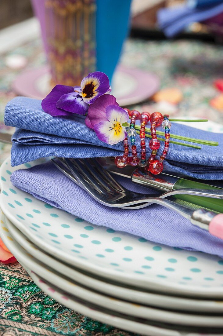 Violas and blue linen napkin tied with beaded napkin ring on stack of plates