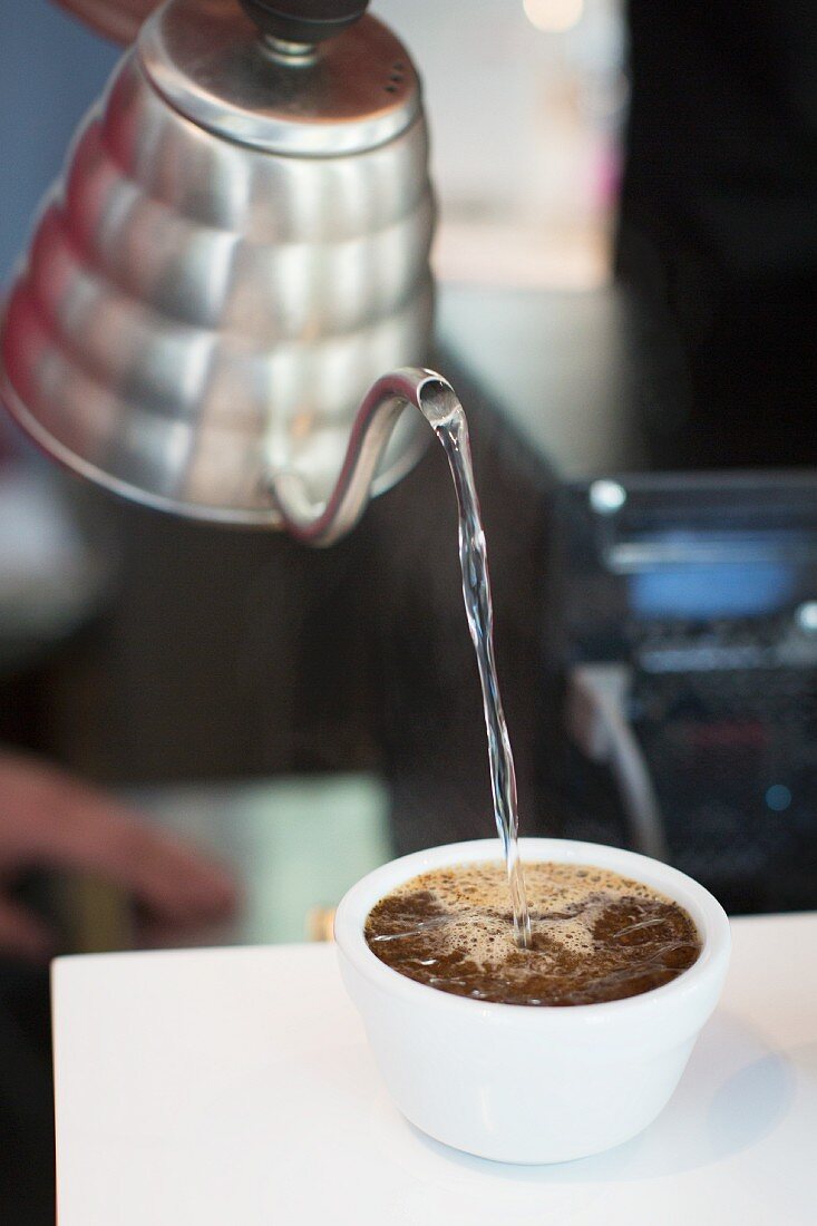 Wasser in Tasse mit Kaffeebohnen gießen