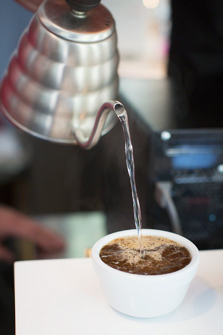 Water being poured into cup of coffee beans