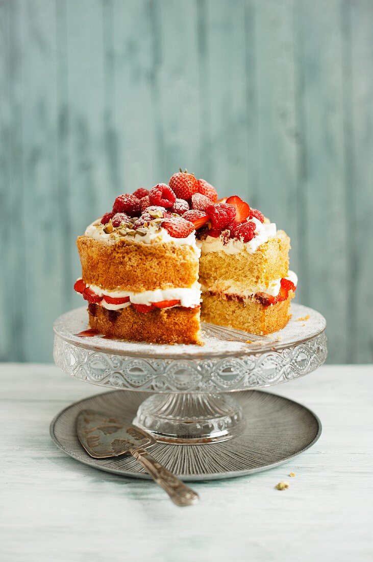 Victoria Sponge Cake mit Sahne, Erdbeeren, Himbeeren und Pistazien auf Tortenständer