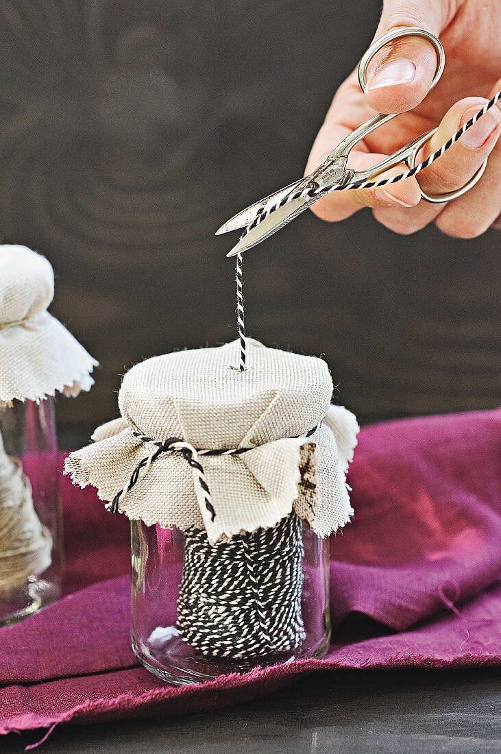 Old jam jars used as string dispensers; hand holding scissors