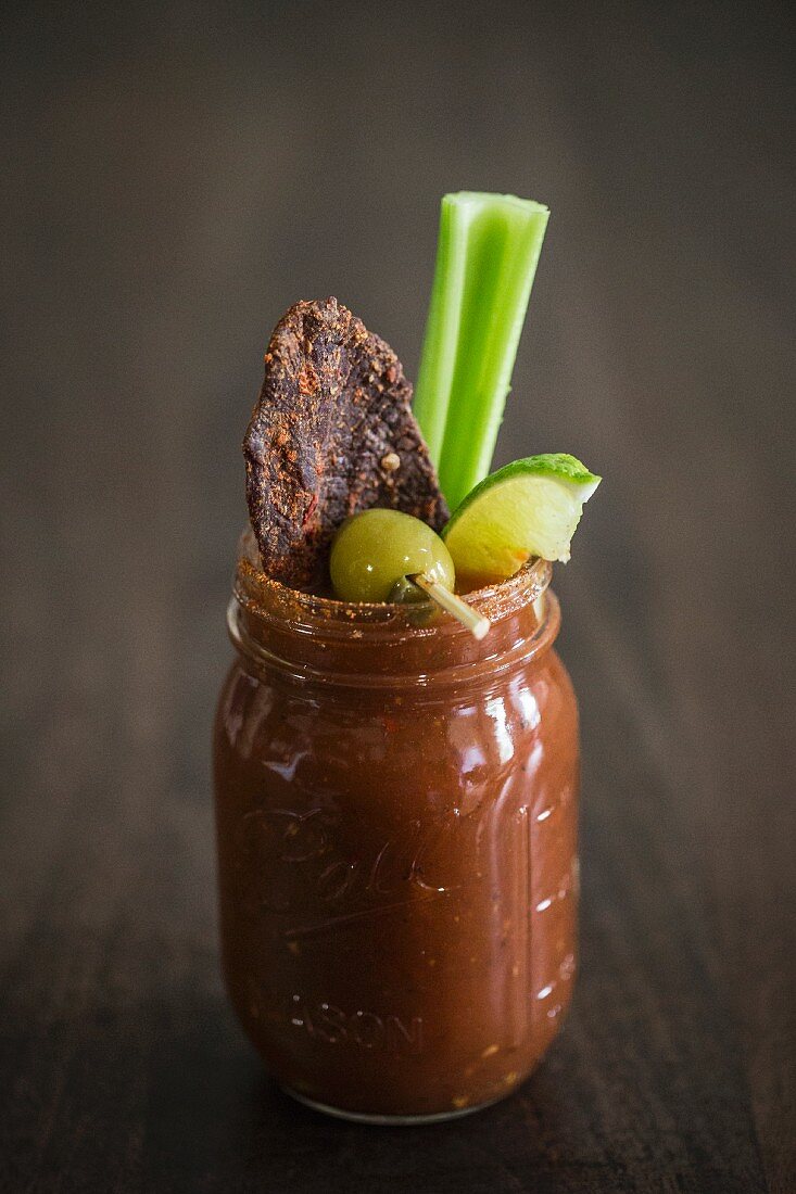 A Bloody Mary with beef jerky, an olive, lime and a stick of celery