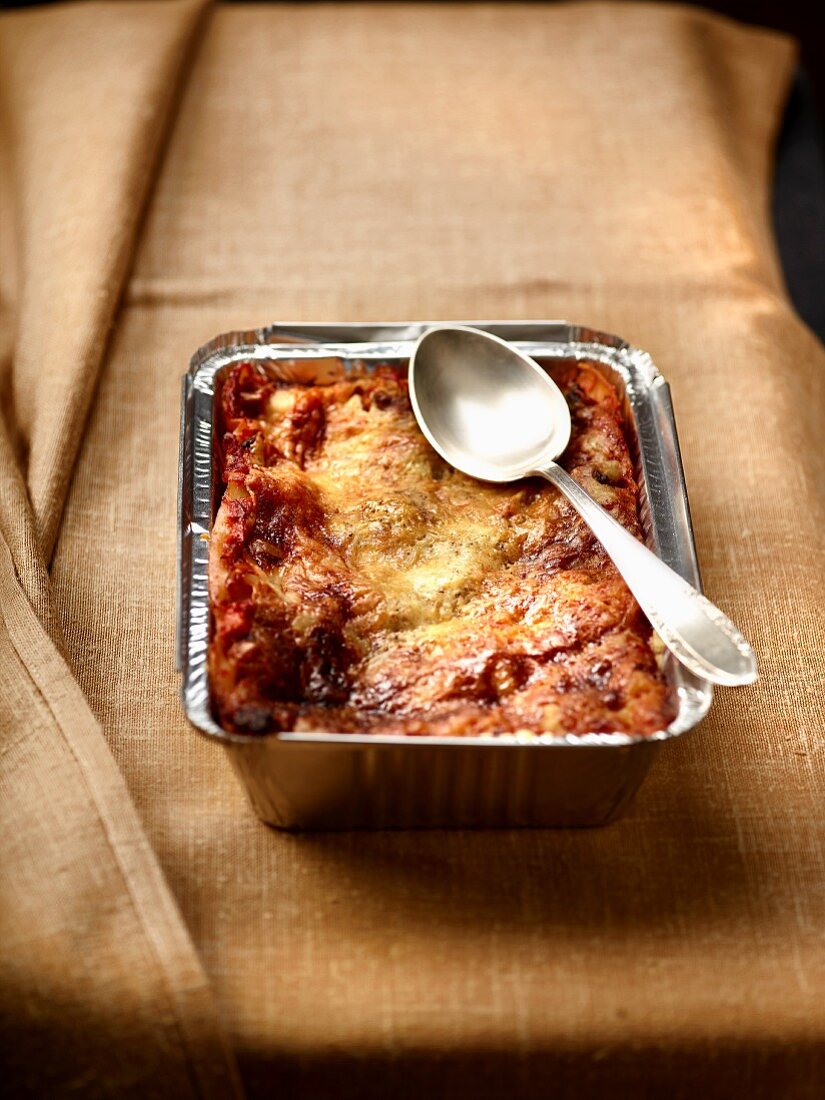 Lasagne with tomatoes and cheese in an aluminium tray with a spoon