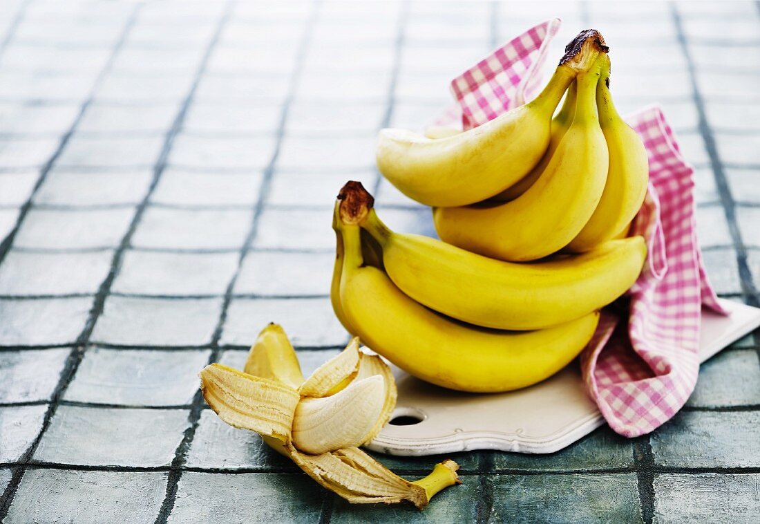Bananas, whole and peeled, on a chopping board with a towel