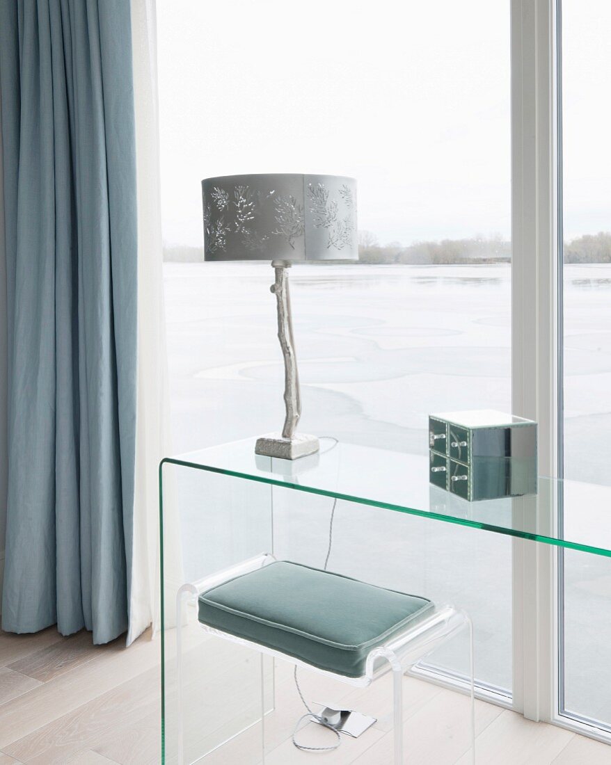Plexi-Hocker mit Sitzkissen und puristischer Konsolen-Glastisch vor Fensterfront mit Seeblick