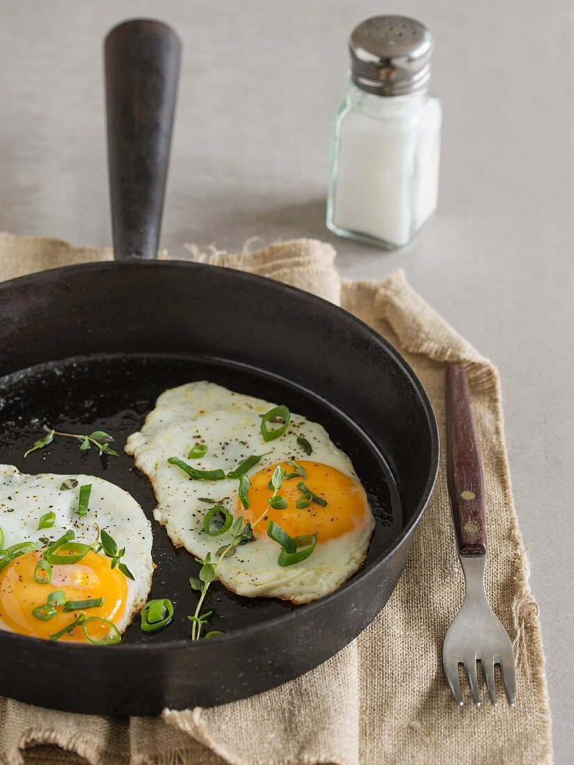 Fried eggs in a pan with fresh thyme