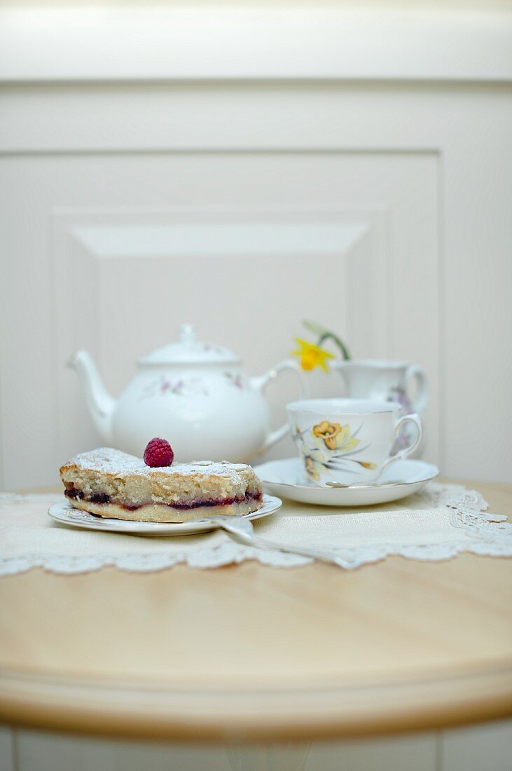 A slice of Bakewell tart (almond and raspberry jam tart, UK) with a vintage teapot and tea cup on a table