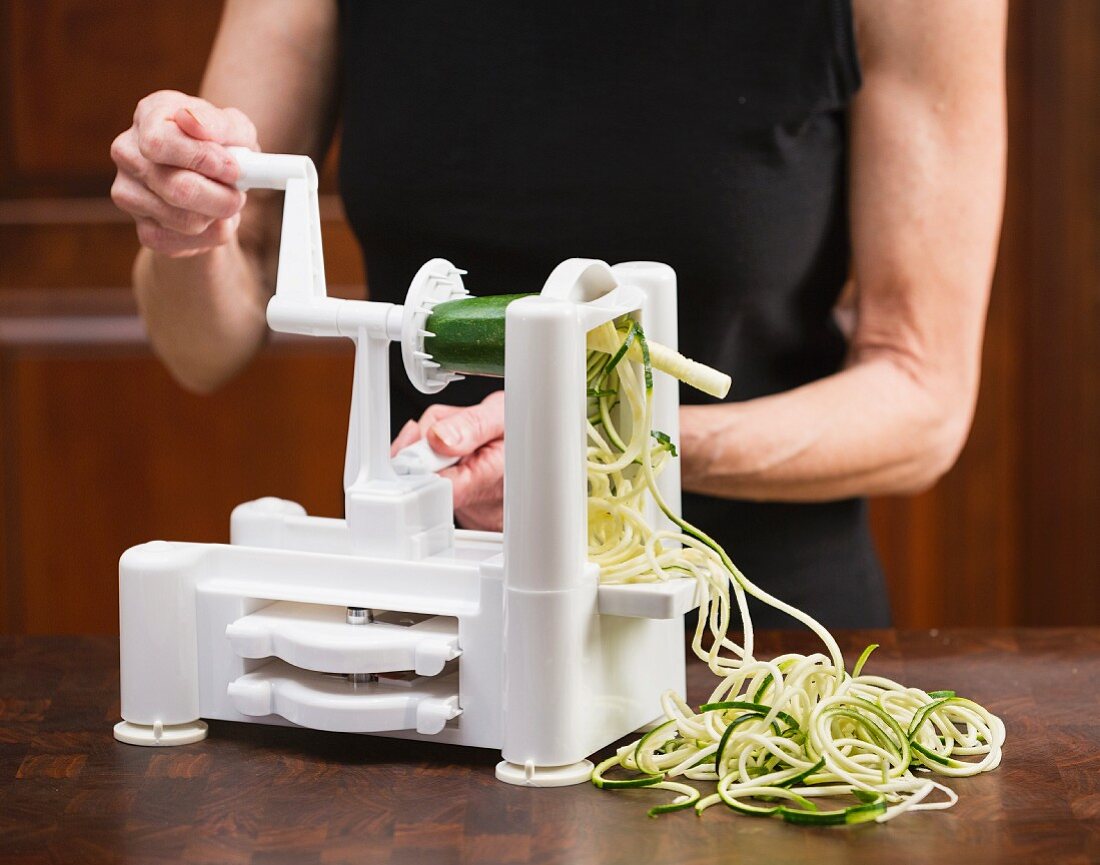 Frau schneidet Zucchinispaghetti mit einem Sprialschneider