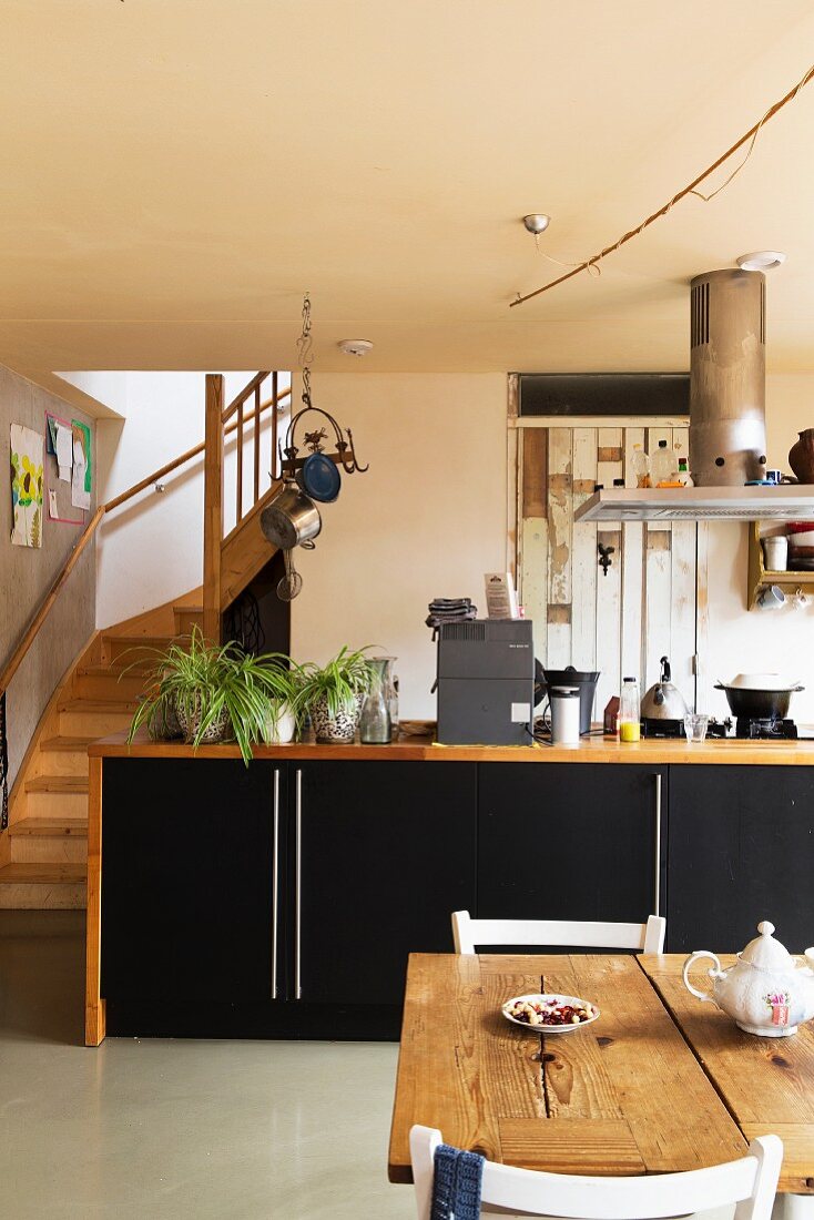 Dining area in front of kitchen counter with wooden frames and black doors; foot of staircase to one side