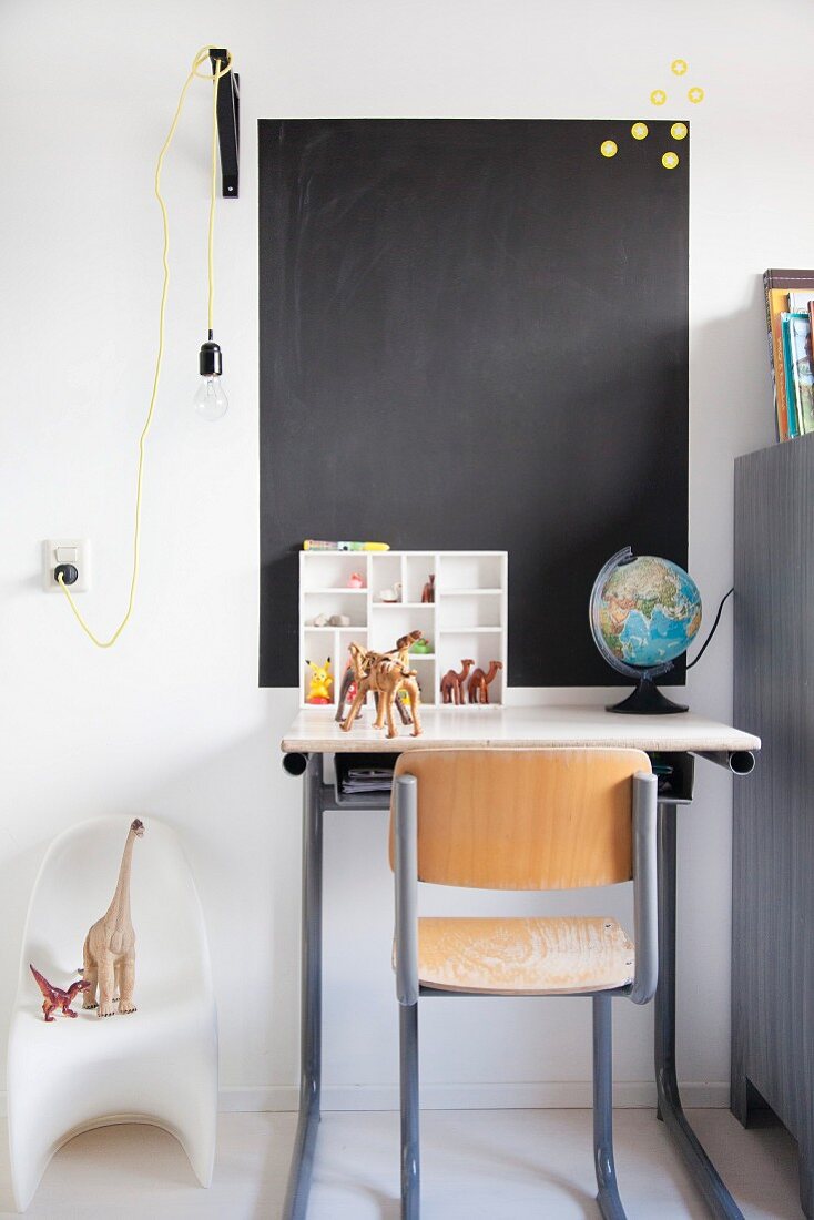 Retro chair, desk, toy dinosaurs, painted chalkboard on wall and pendant lamp with yellow power cable