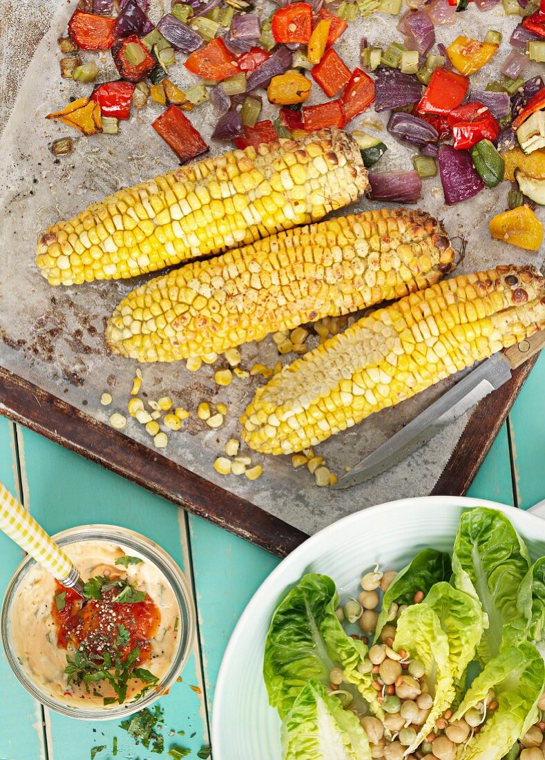 Oven-roasted vegetables and corn cobs with a salad and a dip