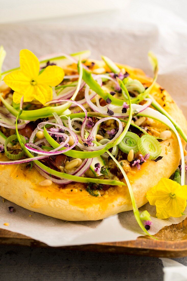 A blind-baked pizza base with grated asparagus, spring flowers, purple onions and pine nuts