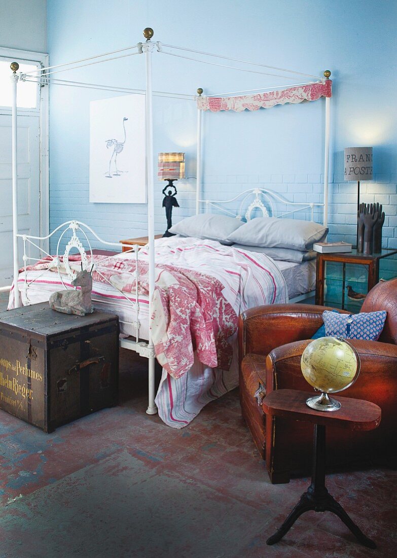 Vintage-style, metal four-poster bed and antique leather armchair in bedroom