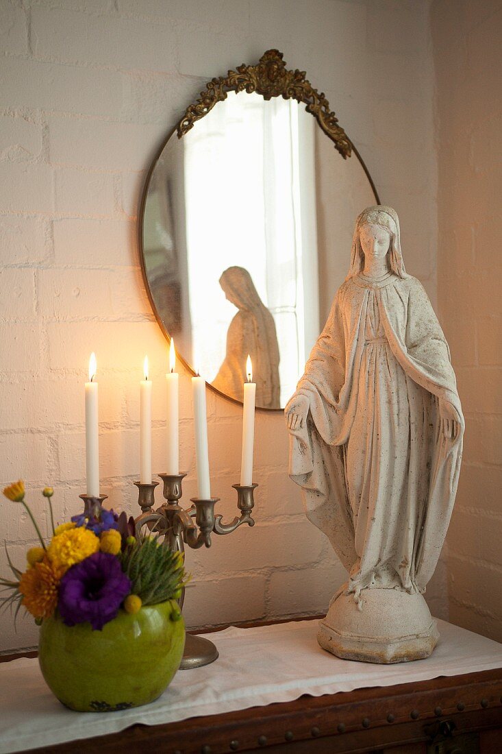 Madonna figurine and brass candelabra on chest of drawers below antique mirror