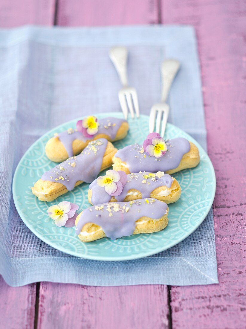 Eclairs mit violettem Zuckerguss und getrockneten Stiefmütterchenblüten