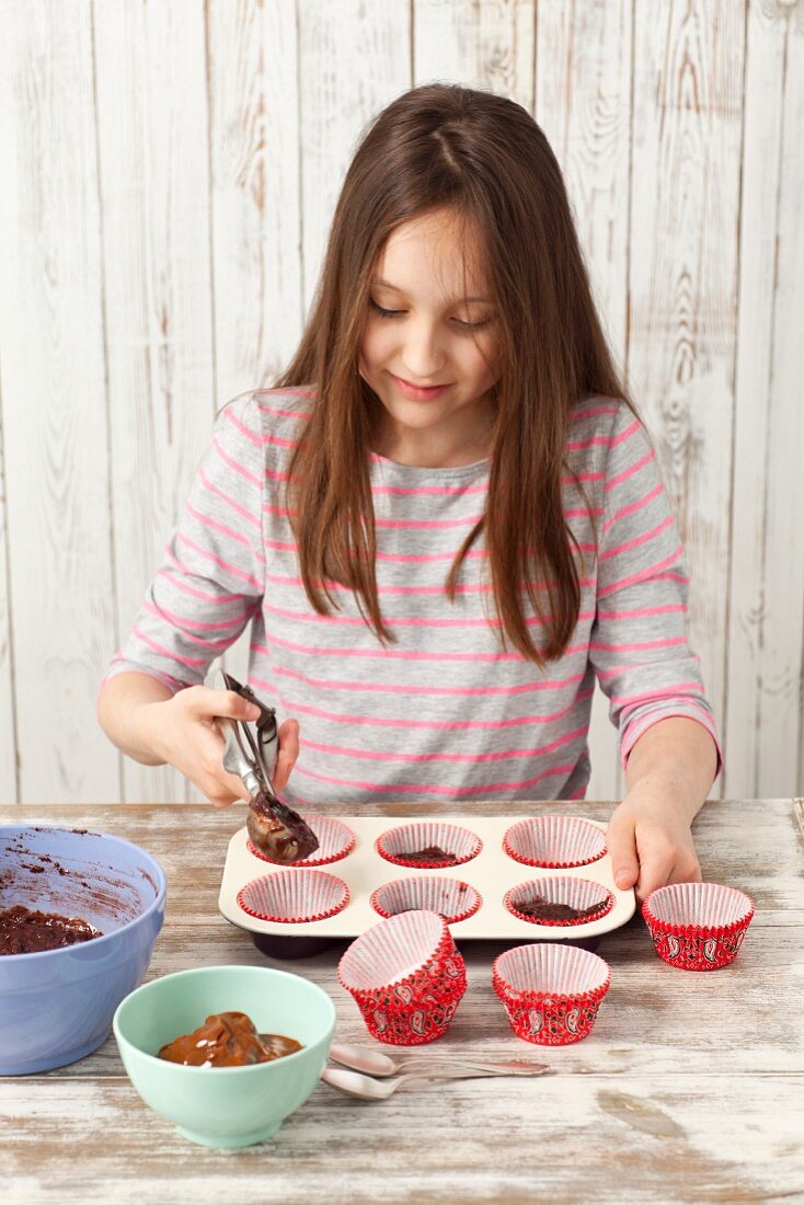 Mädchen bereitet Schokoladencupcakes vor (Teig in Muffinförmchen füllen)