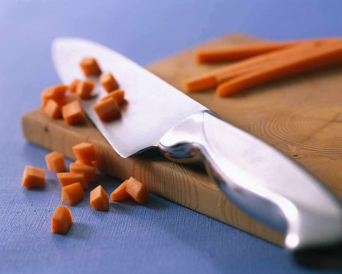 A knife and diced carrots on a chopping board