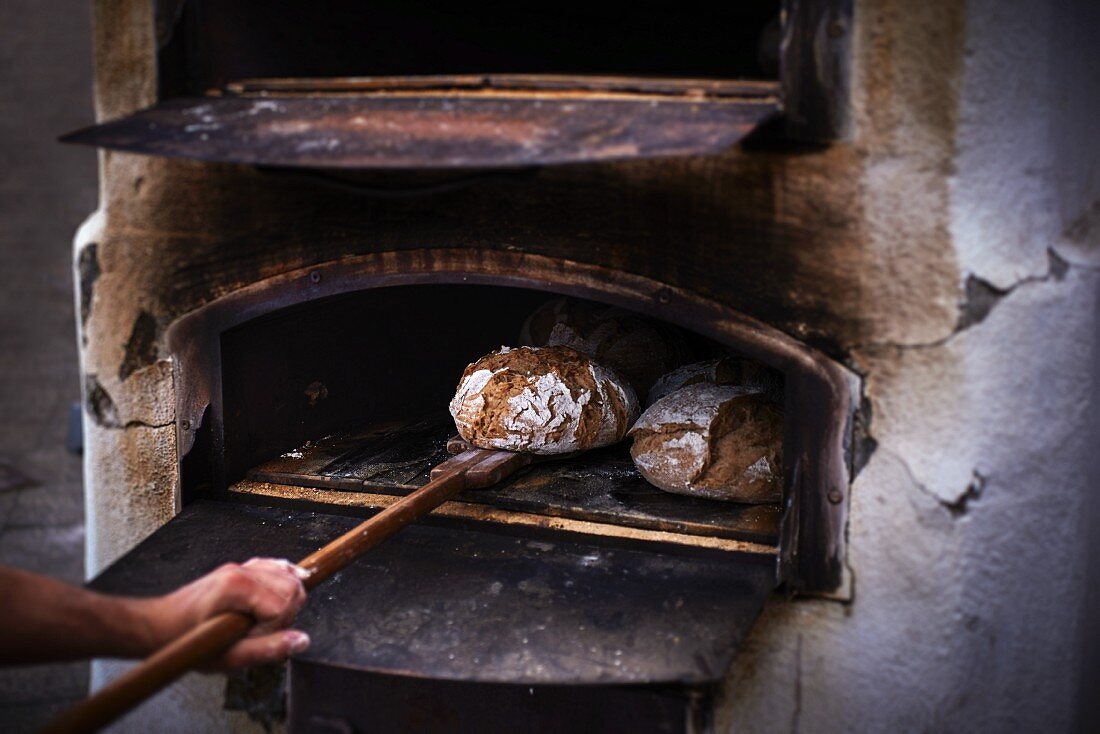 A baker removing a freshly baked loaf of bread from the oven