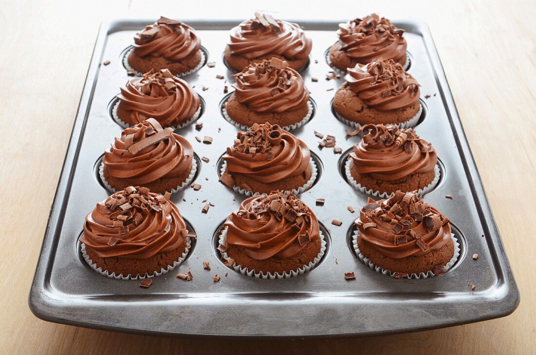 Chocolate cupcakes with butter cream and chocolate curls in a baking tin