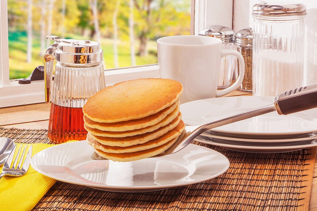 Buttermilk pancakes and maple syrup on a table next to a window