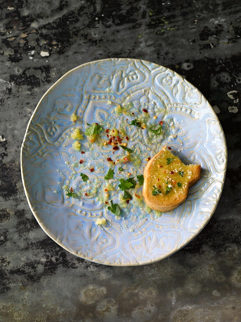 A used plate with the remains of food and a half-eaten slice of grilled bread