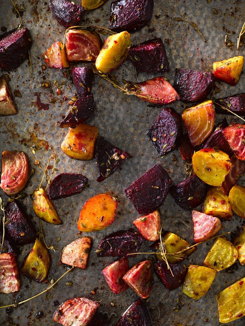 Various types of beets roasted with herbs on a baking tray (seen from above)