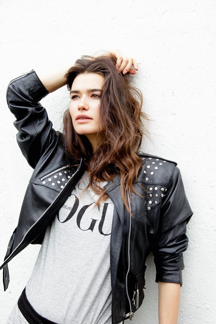 Young woman standing against the white wall wearing a T-shirt and a leather jacket