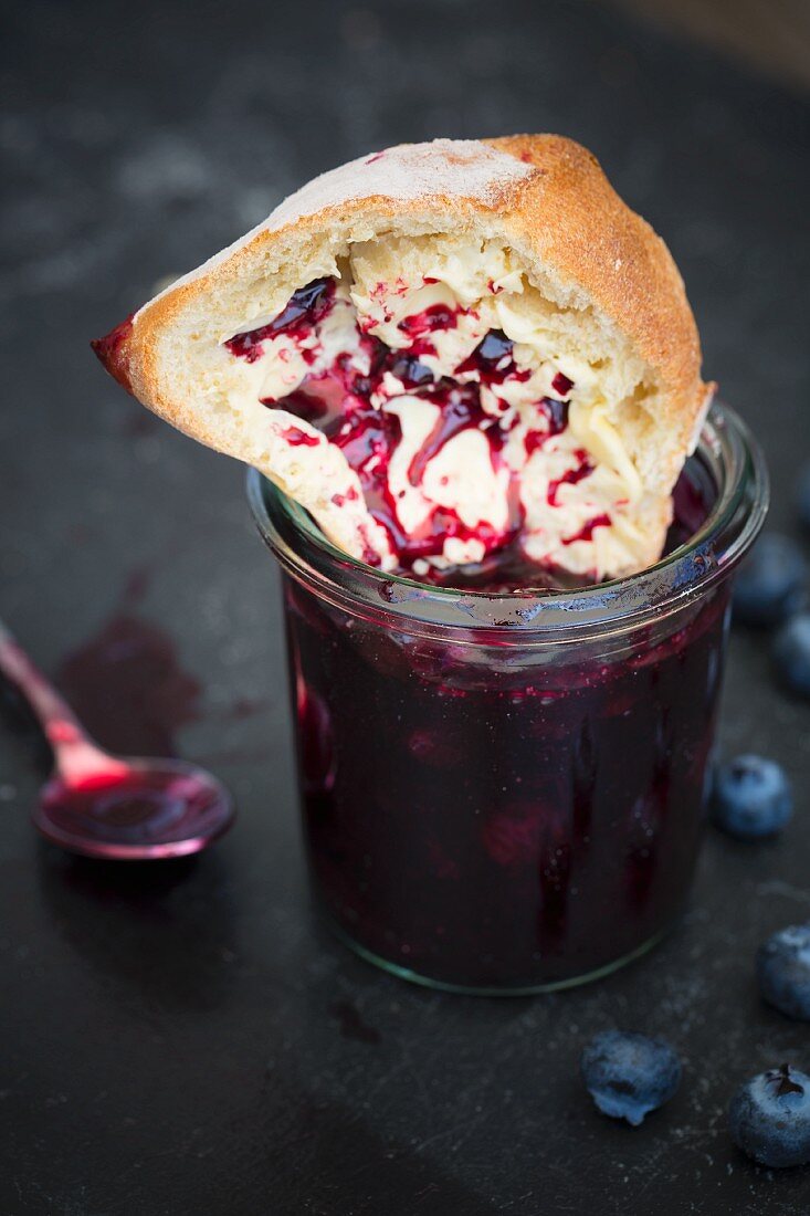 A roll being dipped into a jar of blueberry jam