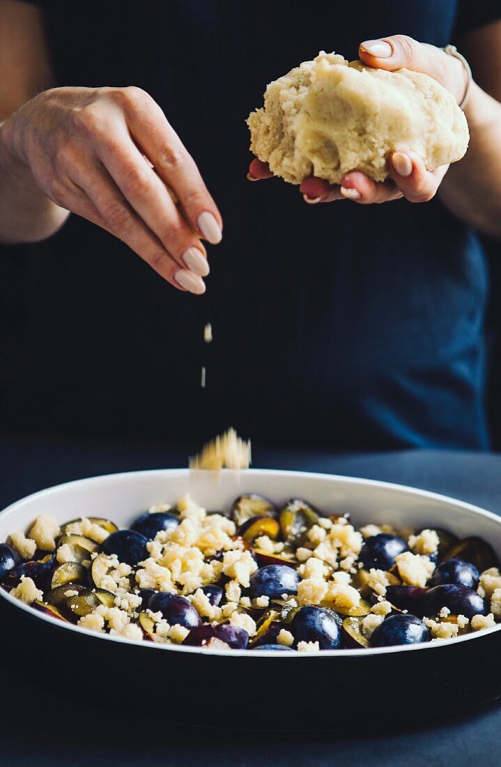 Crumbles being added to a plum crumble