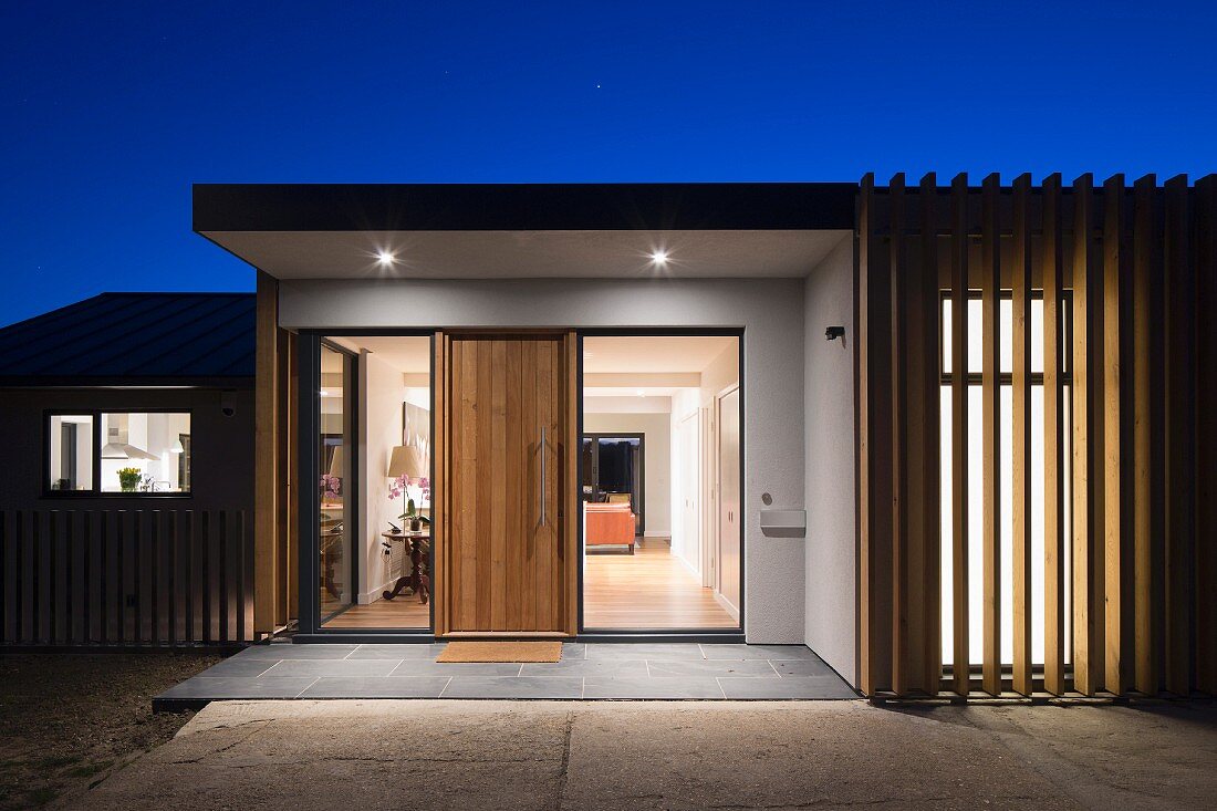 Twilight sky over modern house with illuminated entrance and view of interior