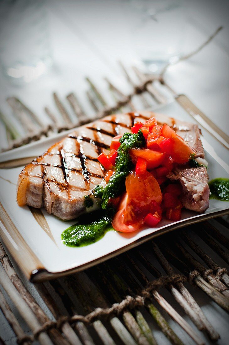 A grilled pork chop with red salsa and pesto sauce