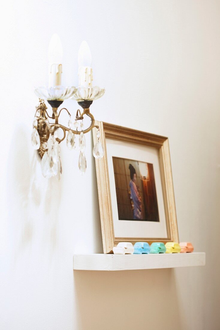 Framed photograph and colourful toy cars on floating shelf next to candle sconce with glass pendants