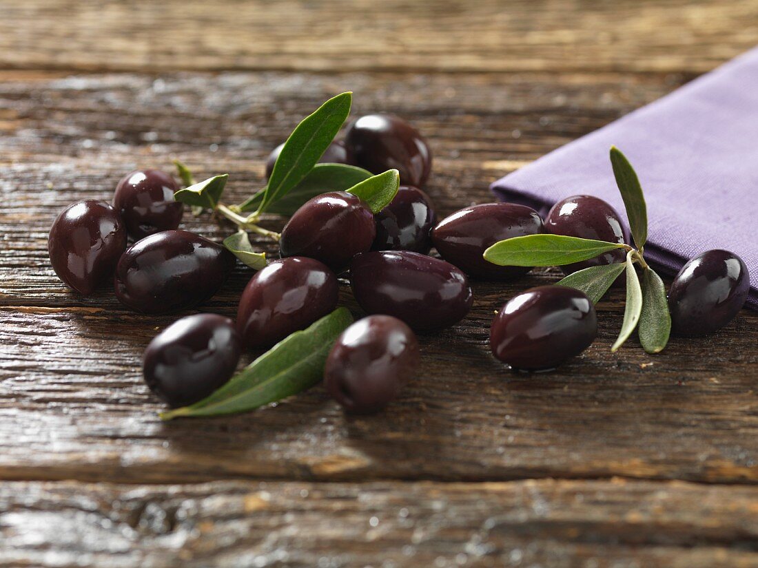 Kalamata olives with leaves on a wooden surface