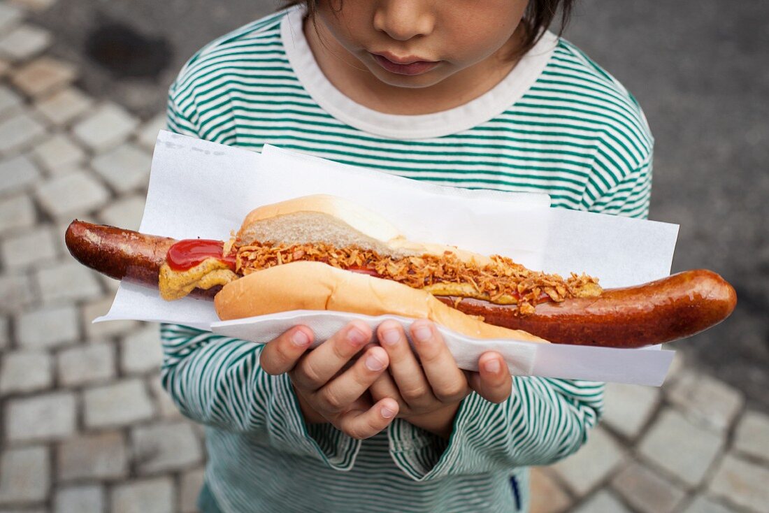 A child holding a giant sausage in a bread roll