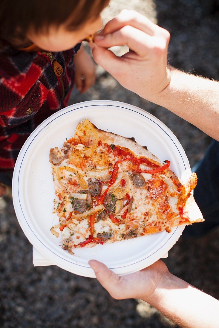 A small child eating pizza on the street