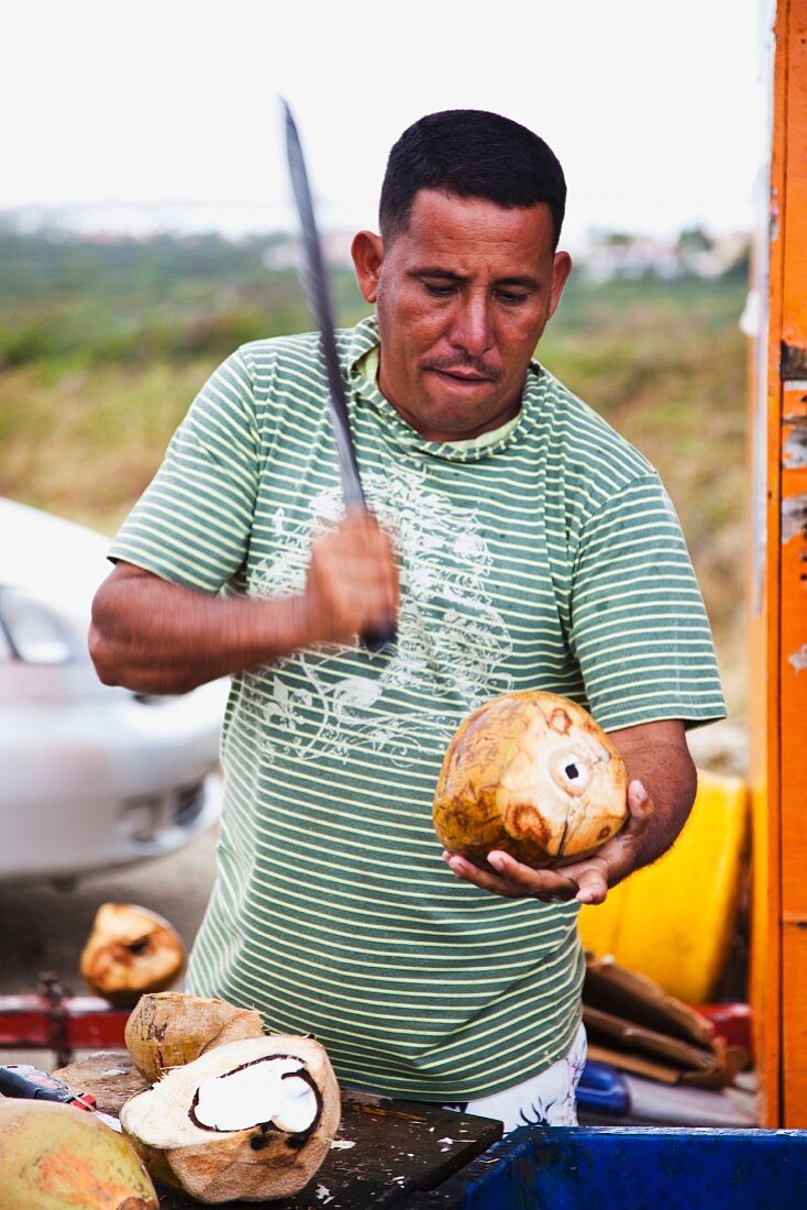 A man opening a coconut with a knife