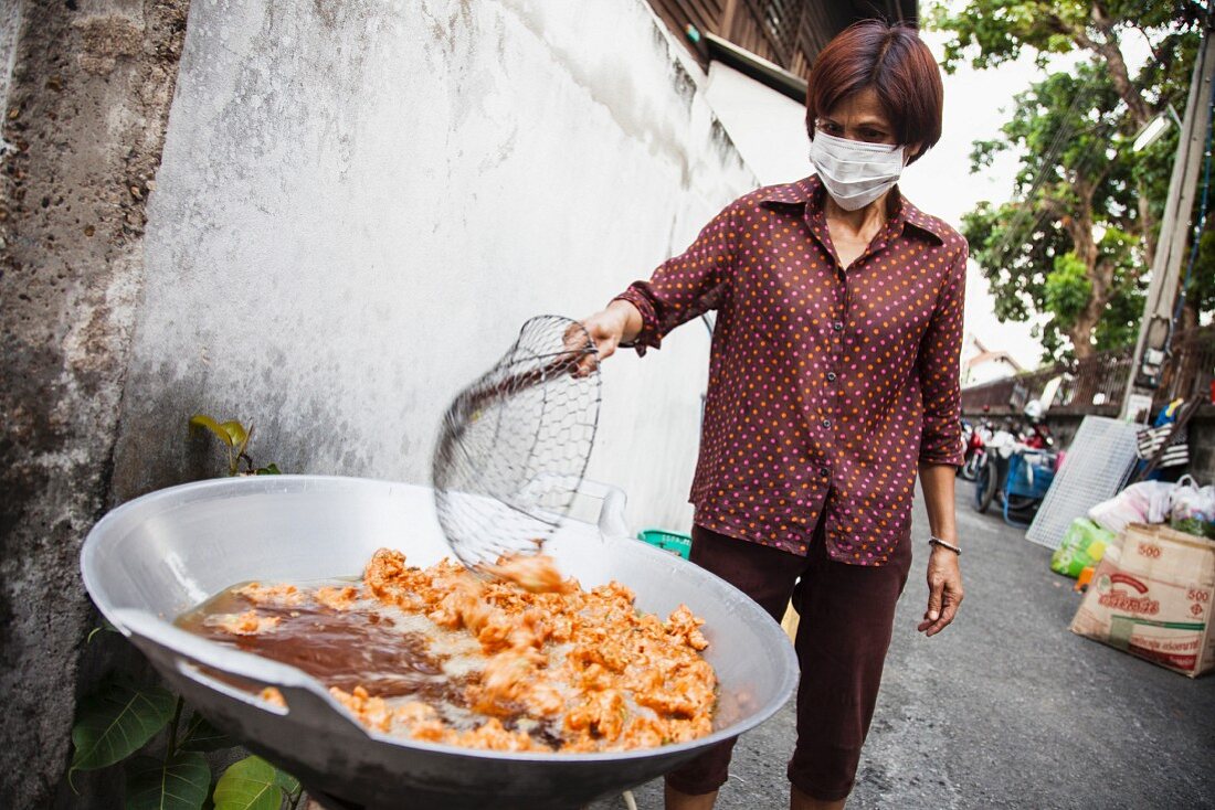 Frau frittiert Hähnchen auf der Straße in Chiang Mai, Thailand