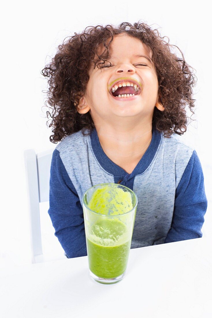 A laughing boy drinking a green smoothie